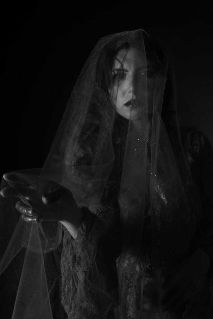 Dramatic black and white portrait of a woman shrouded in a veil, evoking mystery and elegance.
