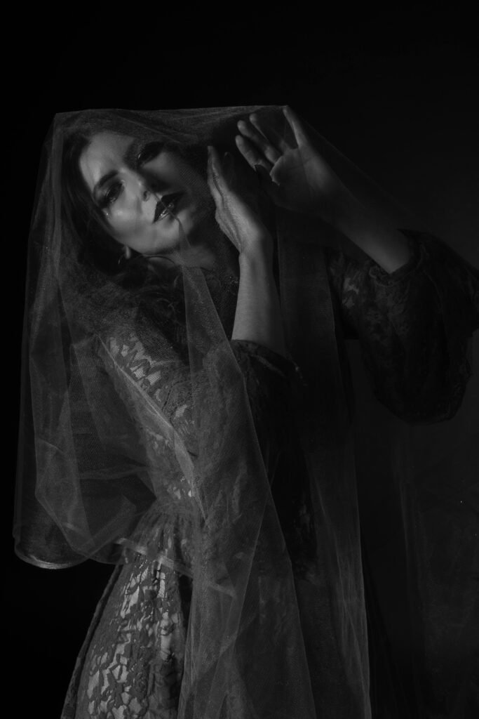 Elegant black and white portrait of a woman draped in lace fabric, creating a moody atmosphere.